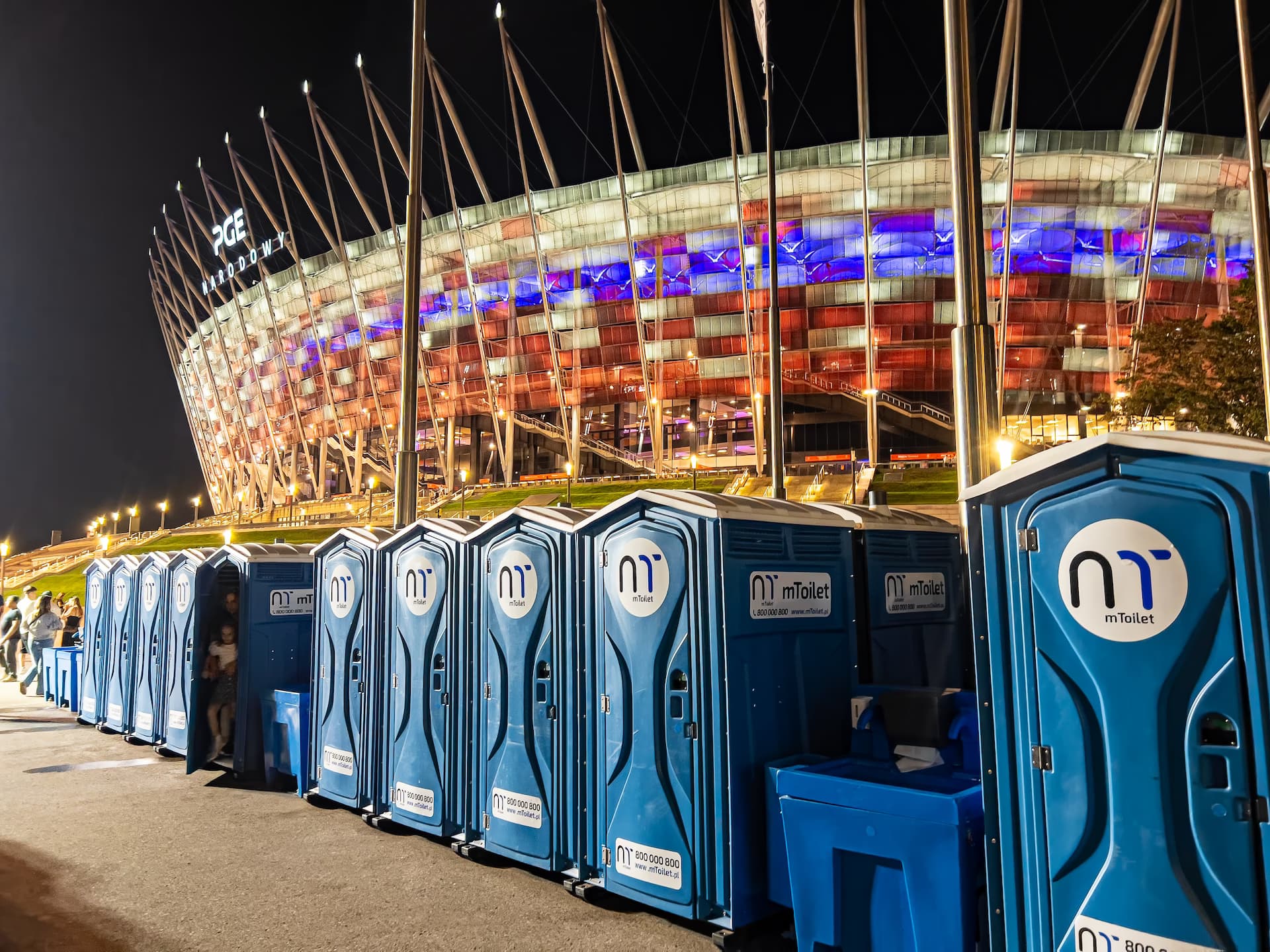 Rząd przenośnych toalet mToilet na tle stadionu w nocy